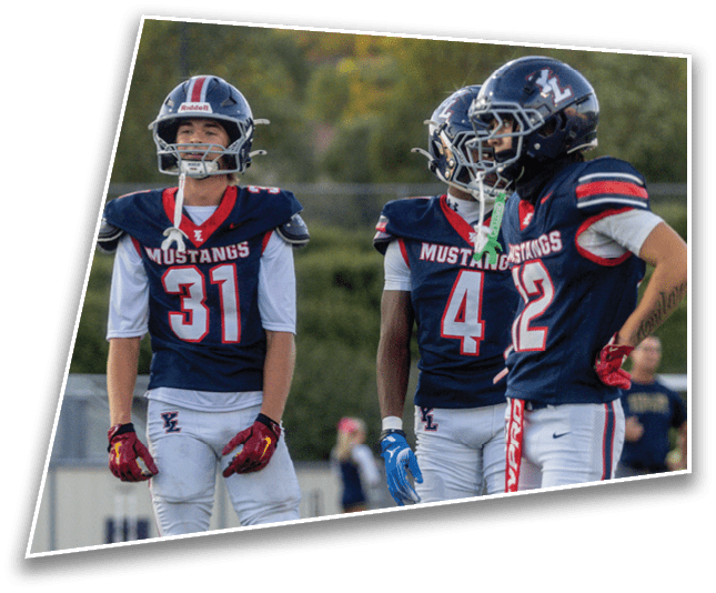 Three people wearing football helmets and Mustangs jerseys are standing outdoors with trees and houses in the background. Description generated by AI