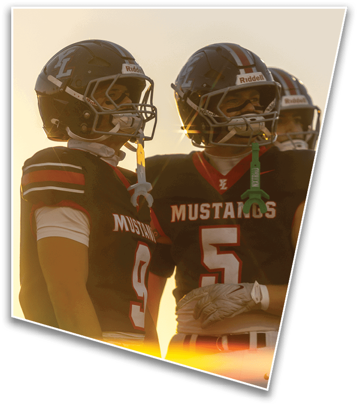 Two people wearing football helmets and black Mustangs jerseys stand side by side with a sunset in the background. Description generated by AI