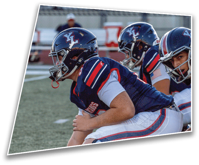 Three people in football uniforms and helmets are crouched on a field, appearing ready for a play. Description generated by AI