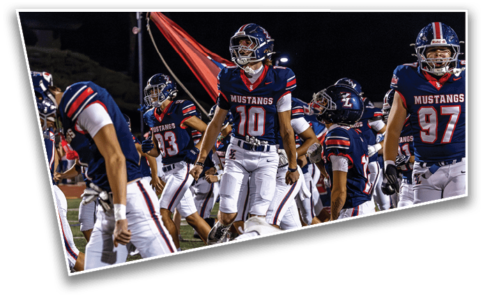 People in football uniforms with helmets and the word Mustangs on their jerseys are gathered on a field at night, some standing and some walking. Description generated by AI