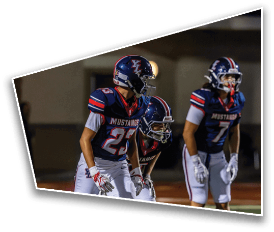 Three people in football uniforms with helmets and gloves are standing on a field in a ready position during a game. Description generated by AI