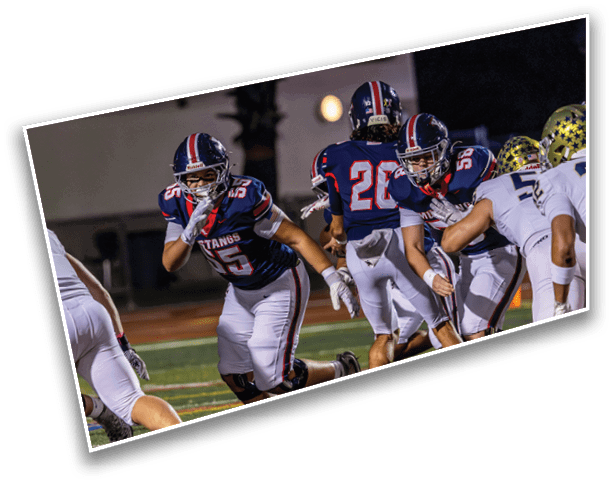 People in football uniforms are actively engaged in a game on a field under stadium lights. Description generated by AI