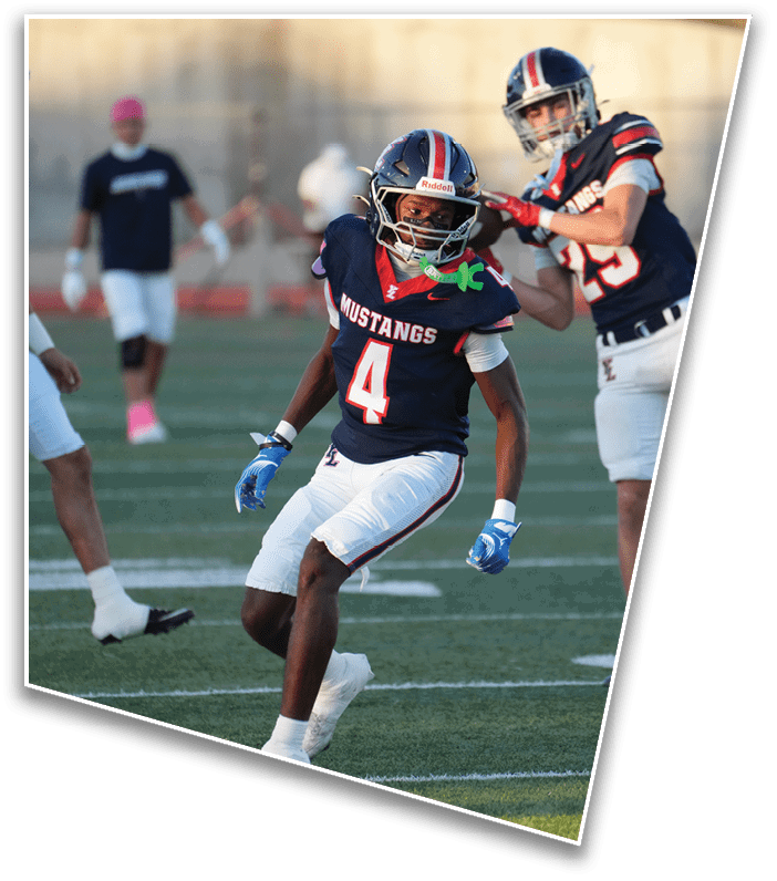 A person wearing a navy blue football uniform with the number 4 and the word Mustangs is running on a football field during a game. Description generated by AI