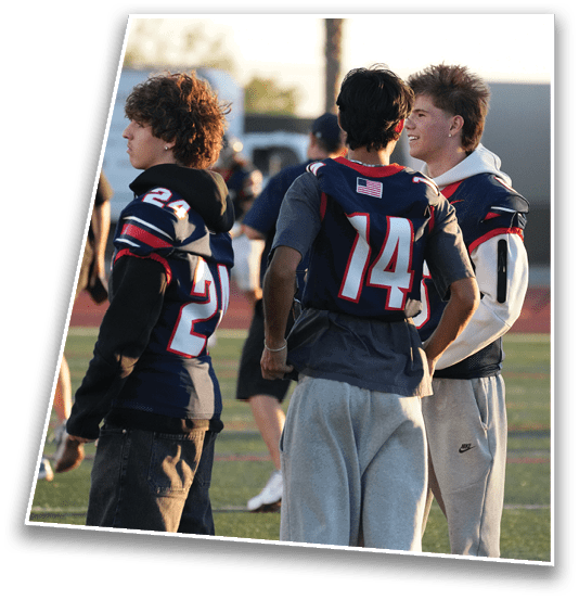 Two people wearing sports jerseys are standing close together outdoors, with one person smiling and the other facing away. Description generated by AI