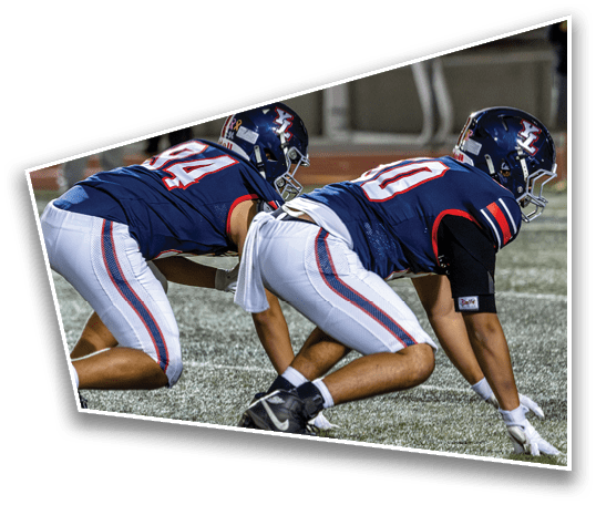 Two people in athletic gear are crouched in a ready position on a sports field, preparing for action. Description generated by AI