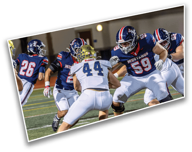 Several people wearing football uniforms are engaged in a play on a field under stadium lights. Description generated by AI