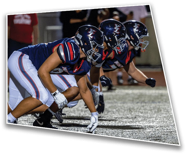 Three people in football uniforms and helmets are crouched in a ready position on a field, preparing for a play. Description generated by AI