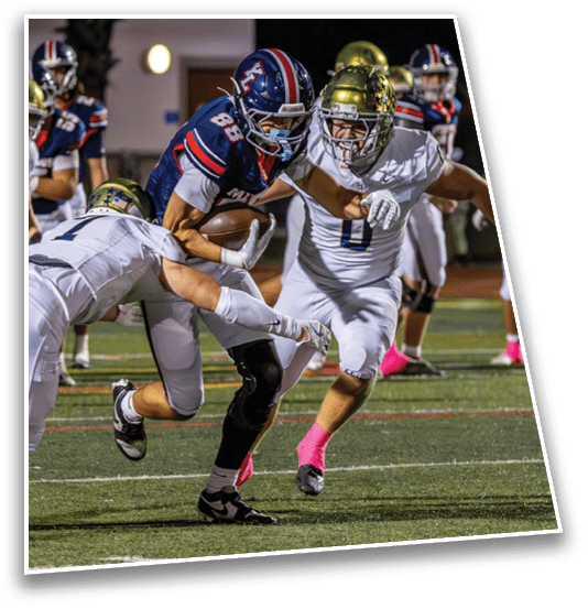 A group of people in football uniforms are actively engaged in a game on a field, with one person in a dark uniform holding the ball while others in white uniforms attempt to tackle. Description generated by AI