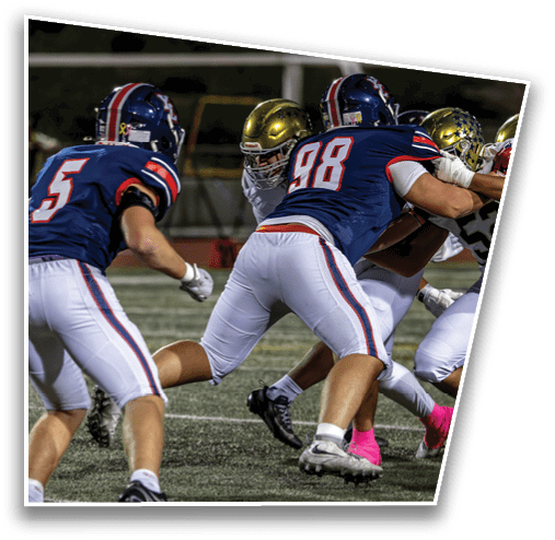 People wearing football uniforms and cleats are engaged in a play on a turf field with some players wearing pink socks. Description generated by AI