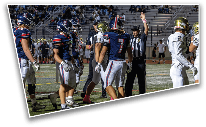 Several people in football uniforms and a referee with a raised arm are on a field during a game. Description generated by AI