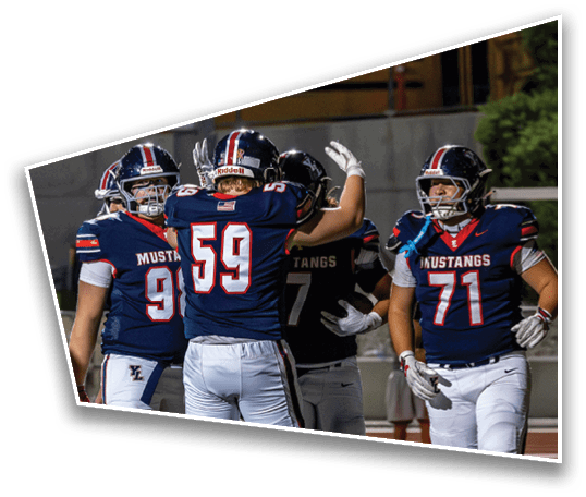 Four football players in navy blue and white uniforms with “Mustangs" on their jerseys are on a field, with two of them appearing to celebrate. Description generated by AI