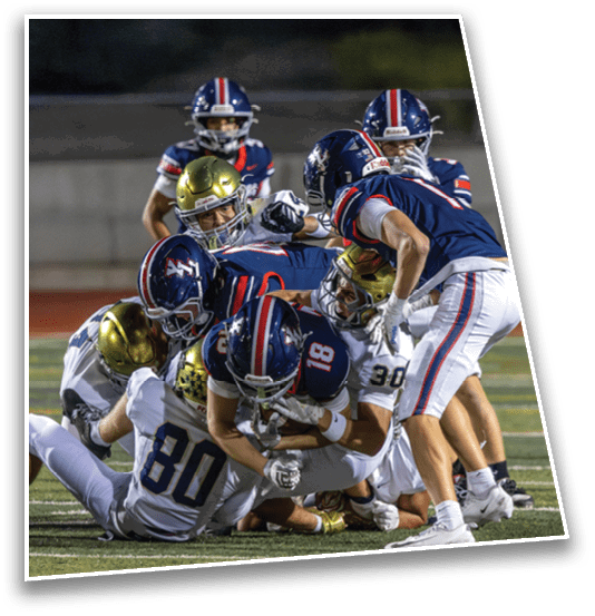 Several people in football uniforms are engaged in a tackle on a grassy field during a game. Description generated by AI