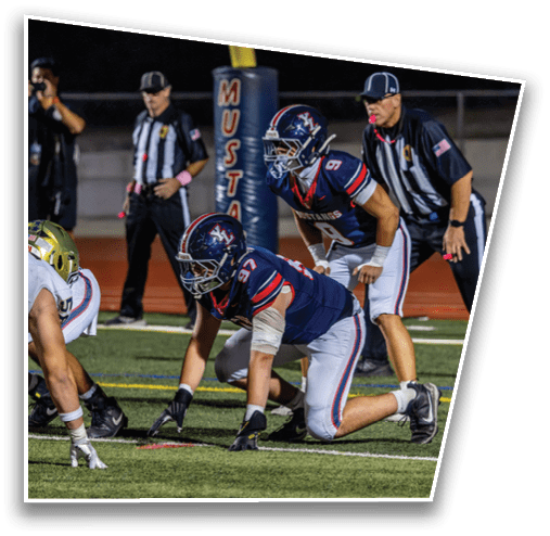 People in football uniforms are lined up on a field preparing for a play during a game. Description generated by AI