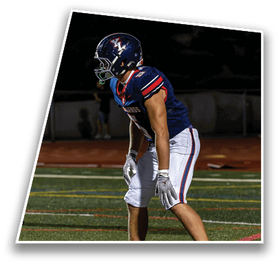 A person wearing a dark blue football uniform and helmet is standing in a ready position on a football field at night. Description generated by AI