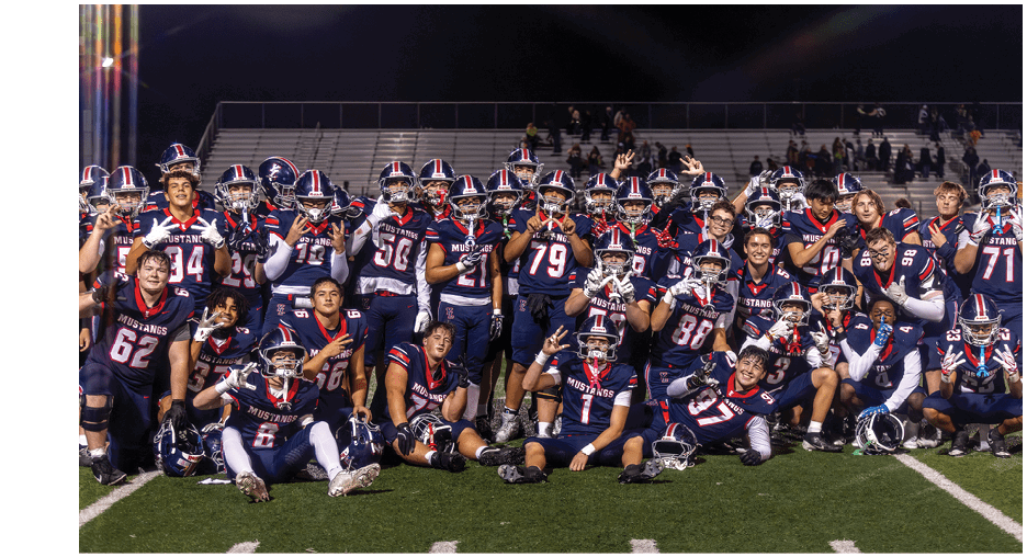 A group of people wearing matching football uniforms pose together on a field at night with some sitting and others standing, smiling and celebrating. Description generated by AI