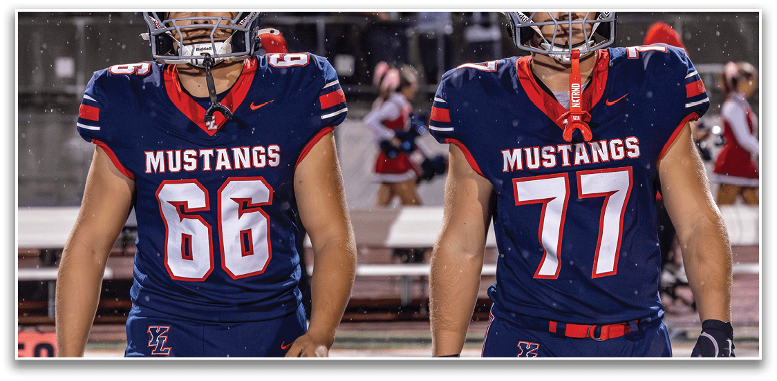Two people wearing dark blue sports uniforms are walking side by side on a field. Description generated by AI