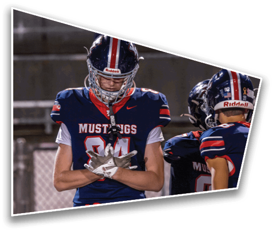 People wearing sports uniforms stand on a field with one person crossing their gloved hands in front of their chest. Description generated by AI