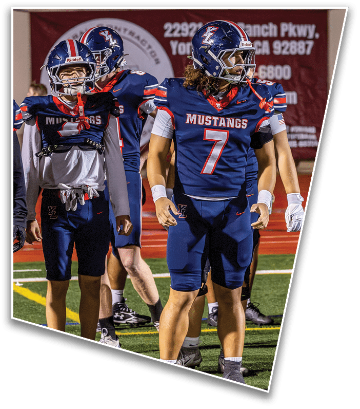 People wearing blue football uniforms with “Mustangs" on the jerseys stand on a football field during a game. Description generated by AI