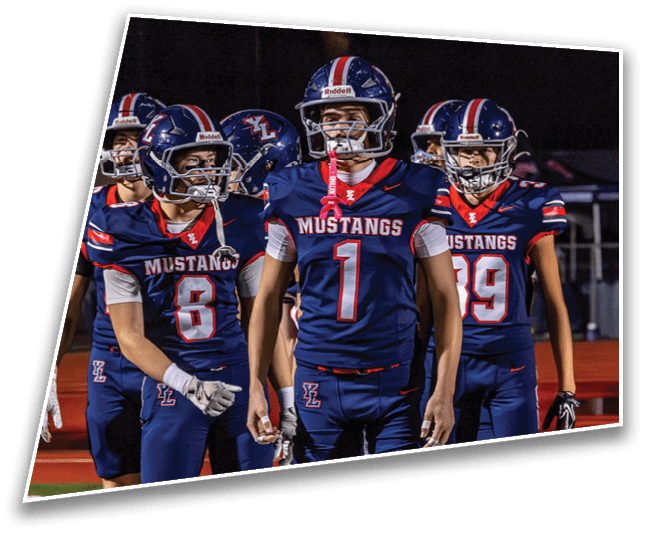 Four people wearing navy blue football uniforms with red and white accents and helmets stand on a field at night. Description generated by AI