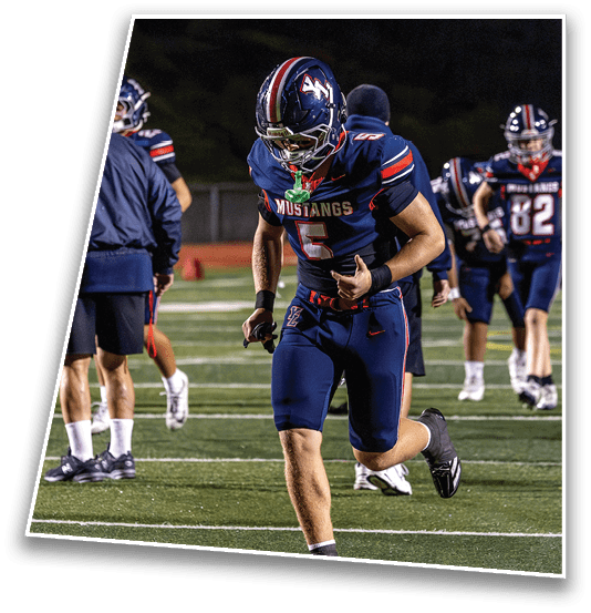 A person in a football uniform with the number 5 and the word Mustangs on the jersey is running on a field with other players and coaches in the background. Description generated by AI