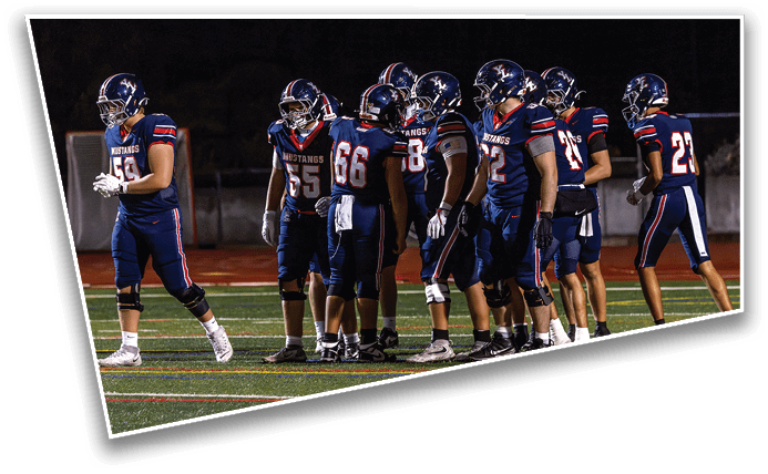 A group of people wearing navy blue football uniforms with helmets are gathered on a field at night. Description generated by AI