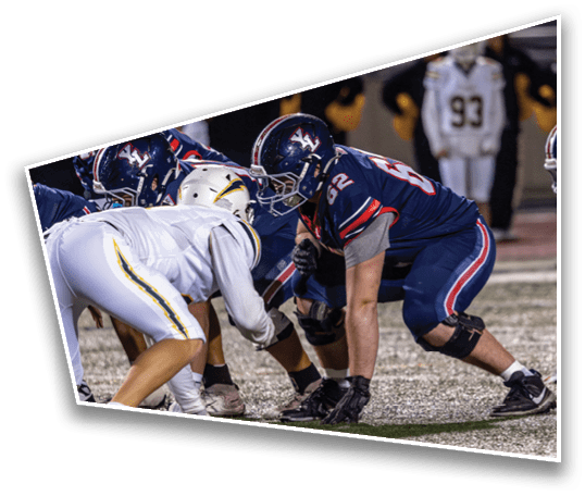 People in football uniforms are crouched on a field, preparing for a play during a game. Description generated by AI