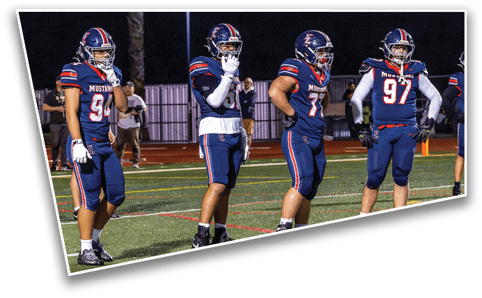Four people in football uniforms stand on a field at night, appearing to be preparing for a play or observing the game. Description generated by AI