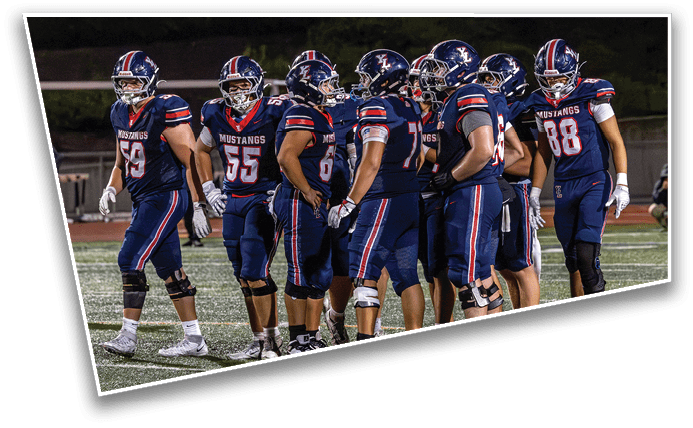 A group of people wearing navy blue football uniforms with helmets are standing together on a field during a game or practice. Description generated by AI