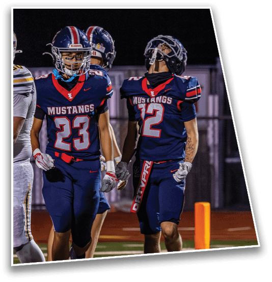 Three people wearing dark blue football uniforms with red and white stripes and helmets stand together on a field at night. Description generated by AI