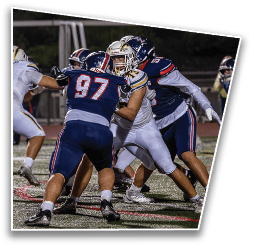 People wearing football uniforms are engaged in a close physical play on a field during a game at night. Description generated by AI