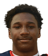Person with short curly hair wearing a sports jersey smiling slightly against a white background. Description generated by AI
