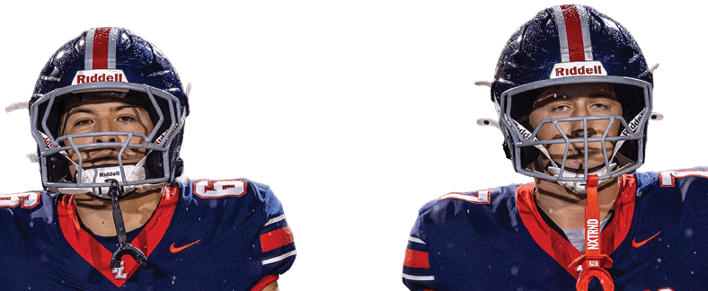 Two adults wearing navy blue football uniforms with “Mustangs" written on the front and helmets are standing side by side on a football field. Description generated by AI