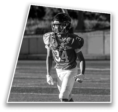 A person wearing a football uniform and helmet is standing on a field, appearing focused and ready for action. Description generated by AI
