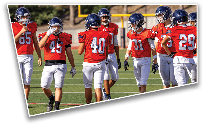 A group of people wearing red sports jerseys and helmets are standing and walking on a football field. Description generated by AI