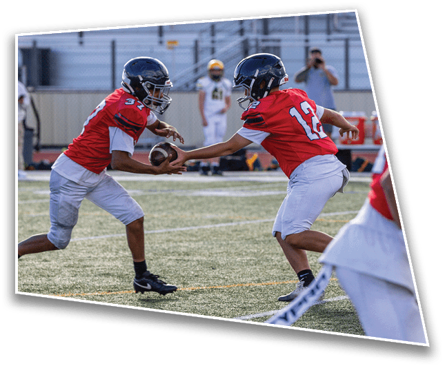 Two people wearing red shirts and white shorts are playing flag football on a grassy field, with one person reaching to grab a flag from the other. Description generated by AI