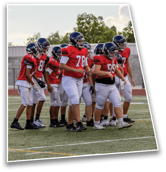 A group of people wearing red football jerseys and helmets are walking together on a sports field under a partly cloudy sky. Description generated by AI