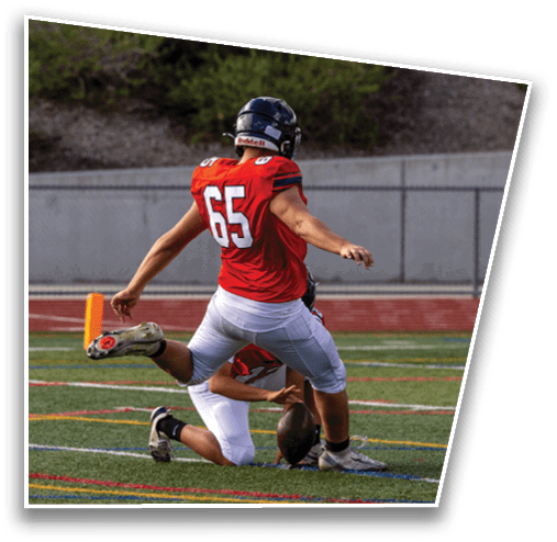 A person wearing a black helmet and an orange sports jersey with the number 85 is seen from behind against a background of green bushes. Description generated by AI