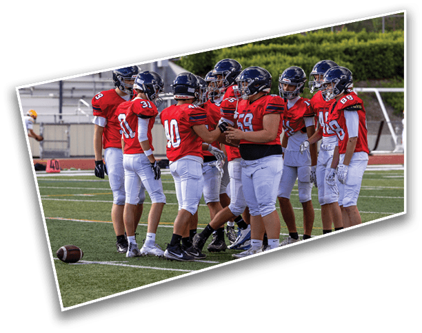 A group of people wearing red football jerseys and helmets are gathered on a football field, seemingly discussing strategy. Description generated by AI