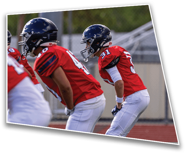 Three people in red football jerseys and helmets are positioned on a field, appearing ready for a play. Description generated by AI