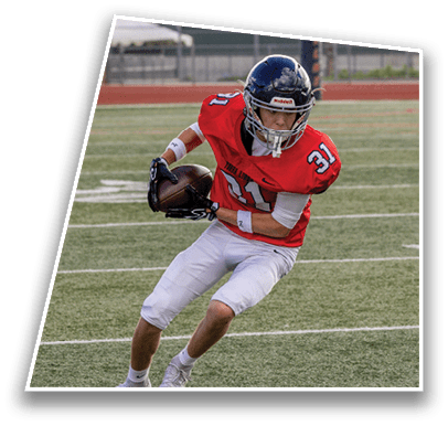 A person wearing a red football jersey and white pants is running on a football field while holding a football. Description generated by AI