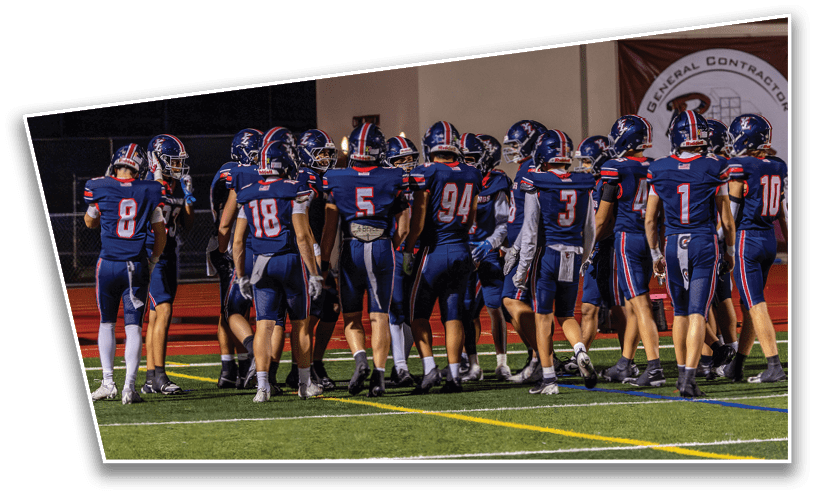 A group of people wearing matching blue football uniforms with helmets are gathered on a field under stadium lights. Description generated by AI