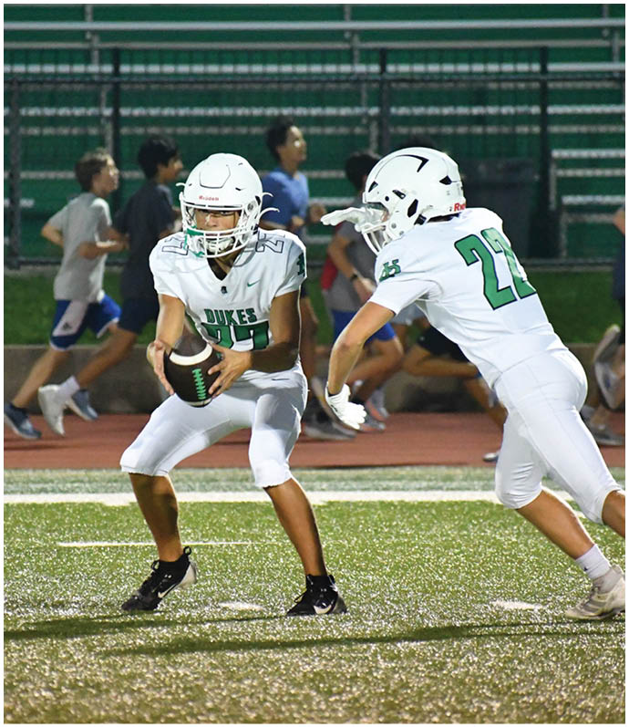 Three football players in blue and white uniforms running on a field. Description generated by AI
