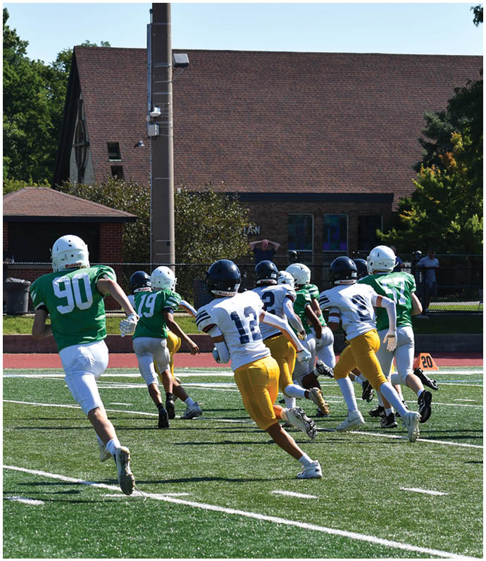 Three football players in blue and white uniforms running on a field. Description generated by AI