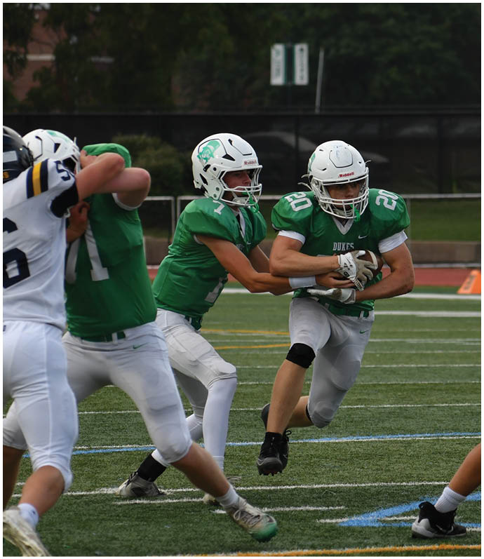 Three football players in blue and white uniforms running on a field. Description generated by AI