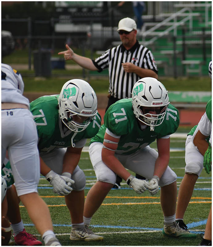 Three football players in blue and white uniforms running on a field. Description generated by AI