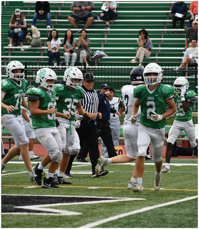 Three football players in blue and white uniforms running on a field. Description generated by AI