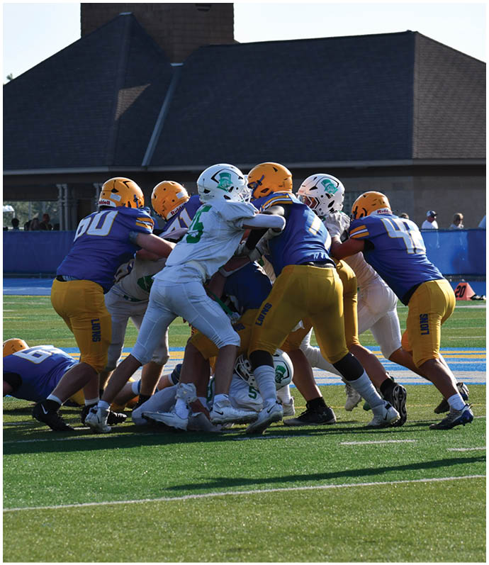 Three football players in blue and white uniforms running on a field. Description generated by AI