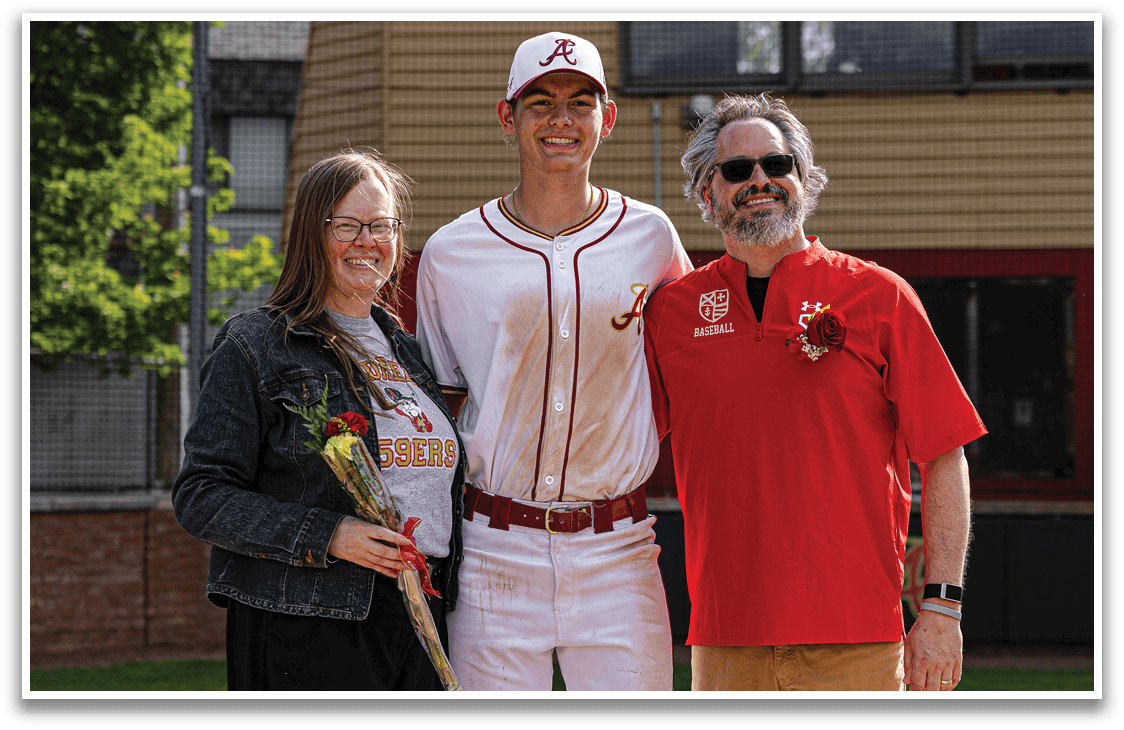 A man wearing a baseball uniform is standing between two people. Description generated by AI