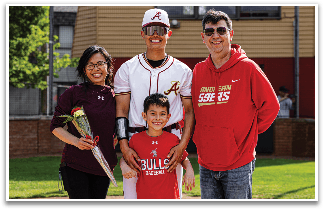 A man, woman, and child pose for a photo in front of a baseball field. Description generated by AI