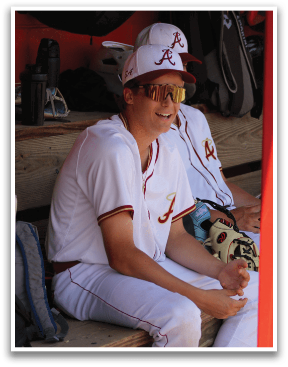 A man wearing a white baseball uniform sitting on a bench. Description generated by AI